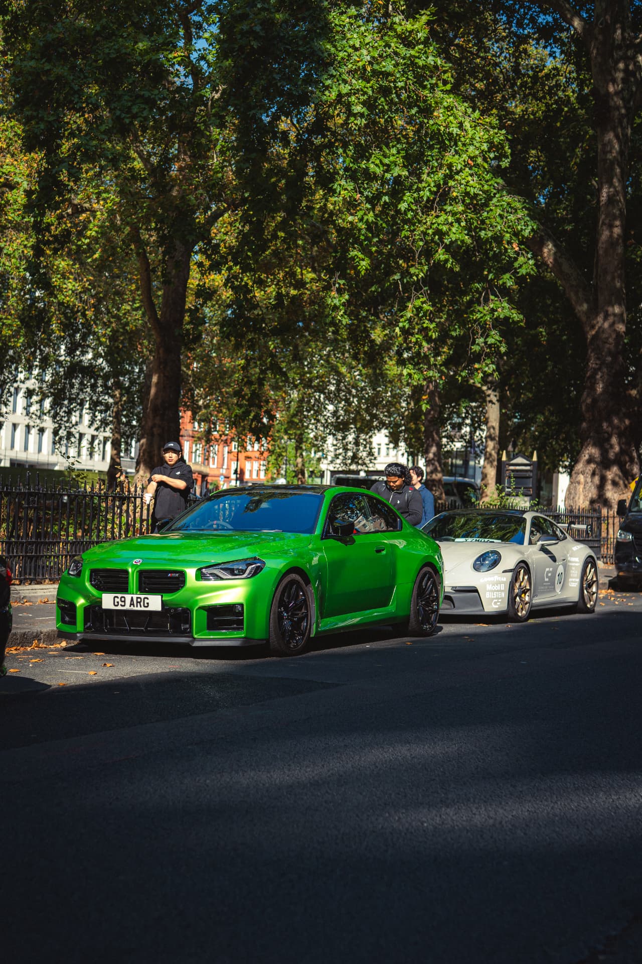 Green BMW M2 and a white Porsche 911 with guests alongside
