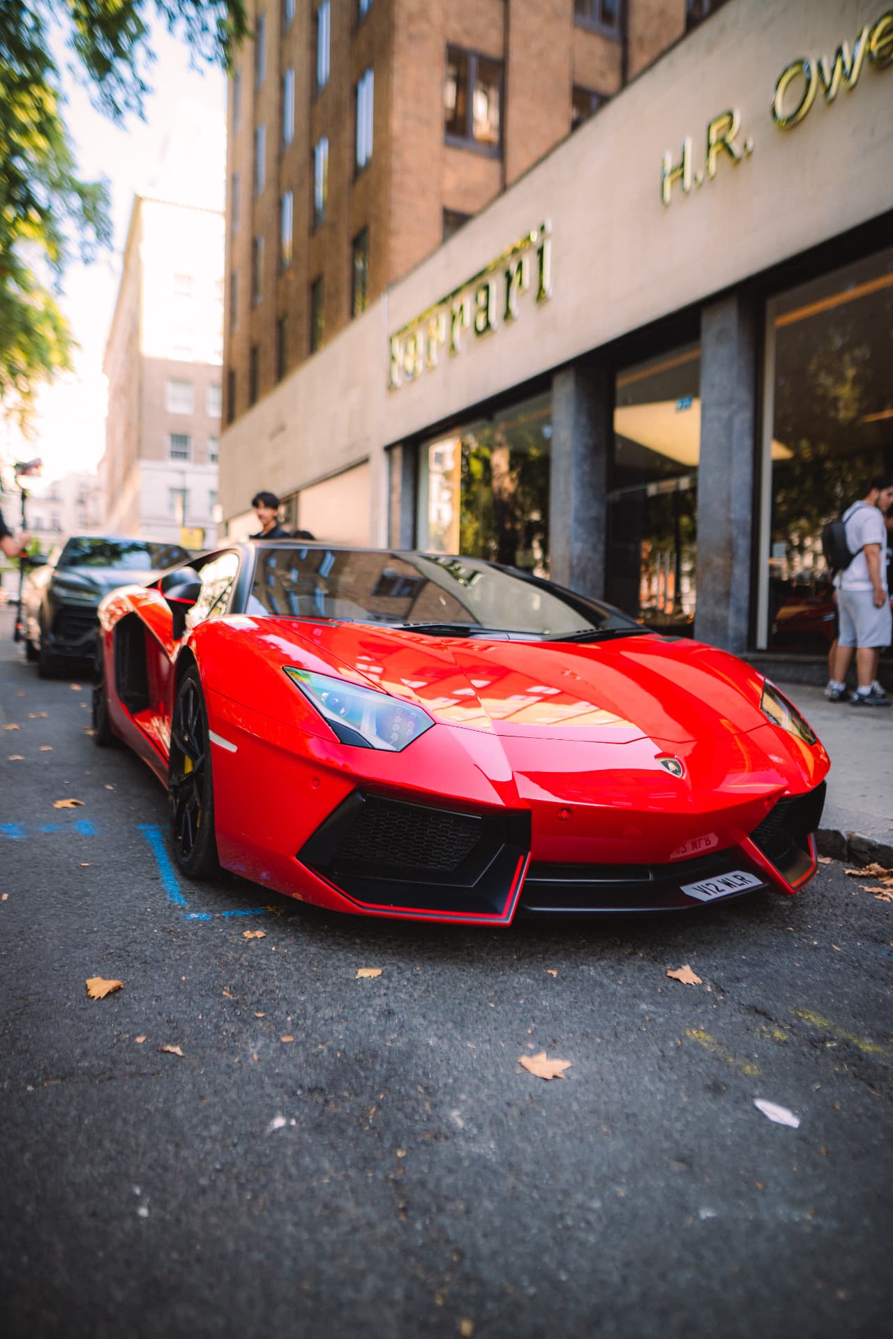 Red Lamborghini Aventador with its doors open outside H.R. Owen Ferrari, surrounded by guests